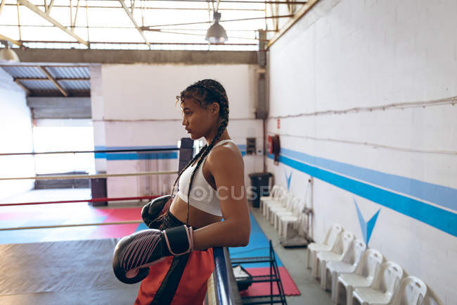 Thoughtful female boxer taking rest in boxing ring at fitness center. Strong female fighter in boxing gym training hard. — Stock Photo