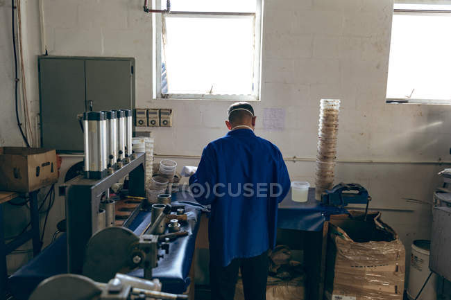 Rückansicht eines Mannes mittleren Alters, der in einer Sportartikelfabrik arbeitet, umgeben von Maschinen. — Stockfoto