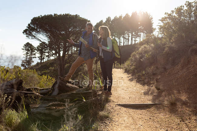 Side view of a mature Caucasian woman and man standing and admiring the view during a hike in the countryside. The man is holding a map, they are both smiling and backlit by sunlight — Stock Photo
