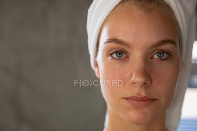 Retrato de perto de uma jovem mulher caucasiana com o cabelo envolto em uma toalha, olhando diretamente para a câmera . — Fotografia de Stock