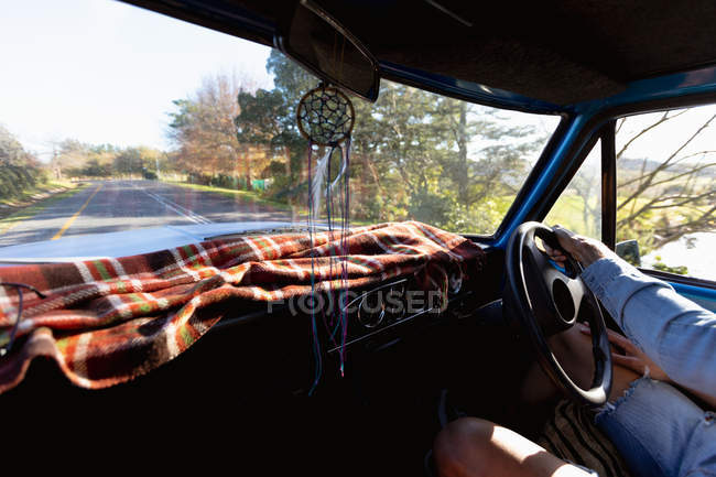 Mid section of man driving a pick-up truck on a rural road trip, with trees in the background and a blanket on the dashboard to block the sun — Stock Photo