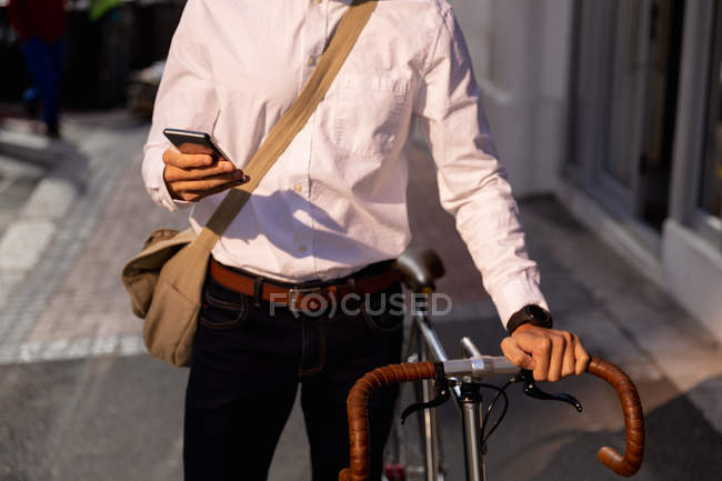 Front view mid section of a man using a smartphone while walking with his bicycle in the city. Digital Nomad on the go. — Stock Photo