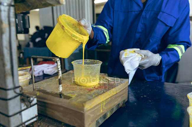 Front view mid section of man working at a cricket ball factory pouring yellow rubber into a plastic container. — Stock Photo