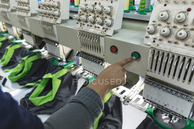 Primer plano de la mano de la mujer que opera una máquina de coser automatizada cosiendo camisas en una fábrica de ropa deportiva . - foto de stock