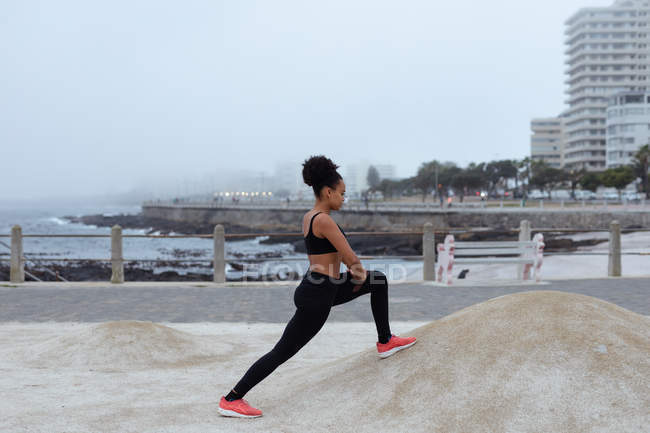 Side view of a young mixed woman wearing sports clothes standing and stretching in an outside urban space — Stock Photo