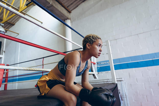 Вид сбоку женщины-боксера отдыхающей в боксерском клубе. Сильная женщина-боец в боксёрском зале тяжело тренируется . — стоковое фото