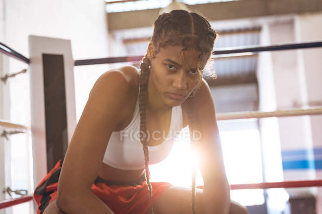 Close-up of female boxer looking at camera while relaxing in boxing ring at fitness center. Strong female fighter in boxing gym training hard. — Stock Photo
