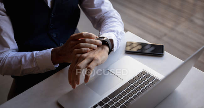 Elevated mid section of man using a laptop and checking the time on his watch, sitting at a table in a cafe. Digital Nomad on the go. — Stock Photo