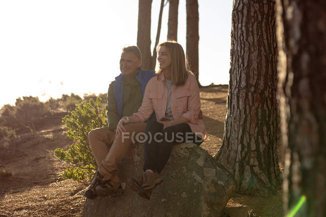 Vista frontal de una mujer caucásica madura y el hombre sentado en una roca juntos admirando el paisaje durante una caminata - foto de stock