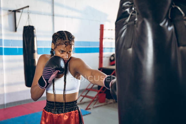 Афроамериканка-боксер, практикующая бокс с боксерской грушей в боксерском клубе. Сильная женщина-боец в боксёрском зале тяжело тренируется . — стоковое фото