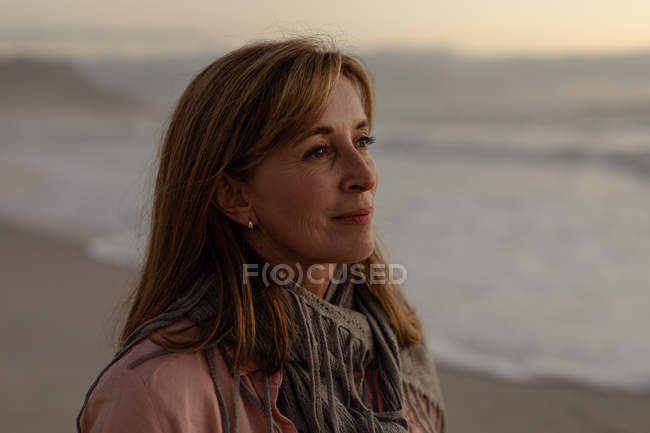 Vista laterale primo piano di una donna caucasica matura che si gode la vista su una spiaggia vicino al mare al tramonto — Foto stock