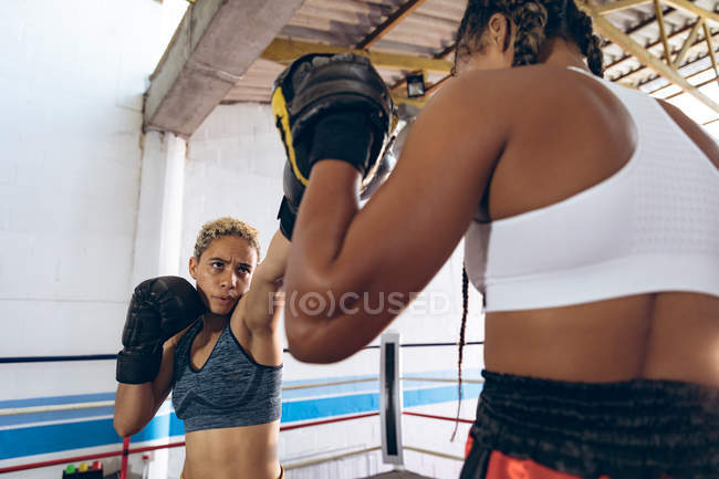 African American trainer assisting female boxer in boxing at fitness center. Strong female fighter in boxing gym training hard. — Stock Photo