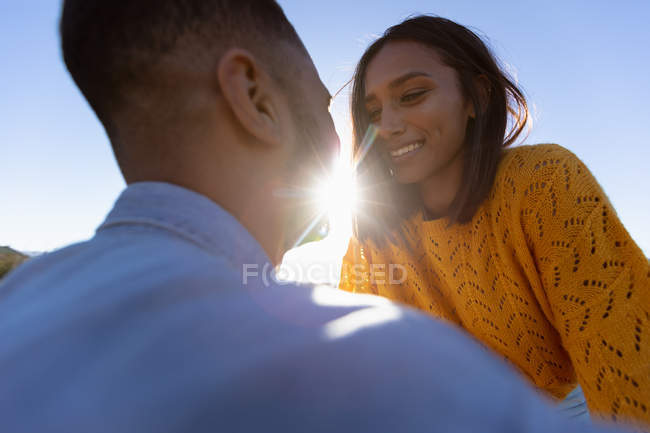 Over the shoulder view of a young mixed race couple enjoying a roadside break during a road trip. She is sitting on the hood of their pick-up truck and they are smiling and about to kiss — Stock Photo
