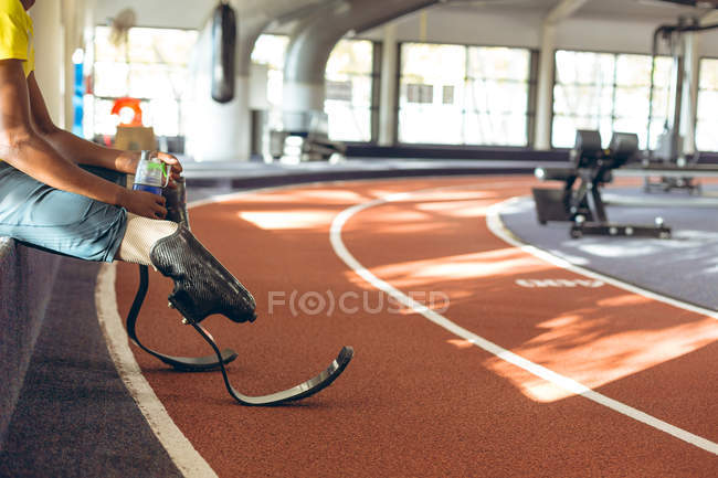 Baixa seção de água potável atlética masculina com deficiência em uma pista de corrida no centro de fitness — Fotografia de Stock