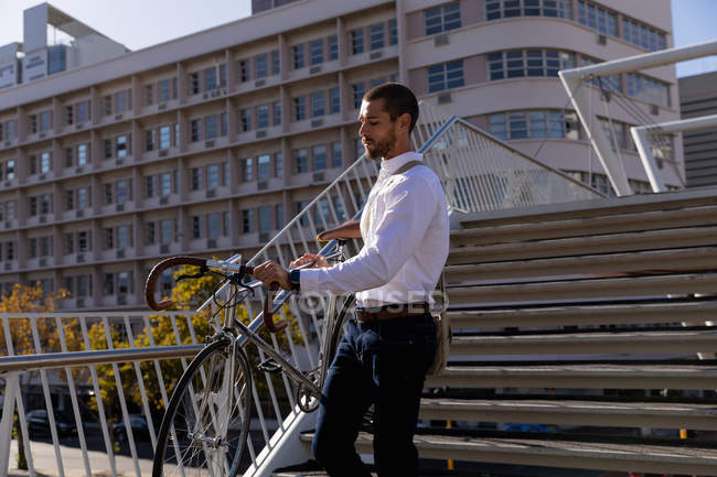 Seitenansicht eines jungen kaukasischen Mannes, der sein Fahrrad die Treppe in der Stadt hinunterträgt. Digitaler Nomade unterwegs. — Stockfoto