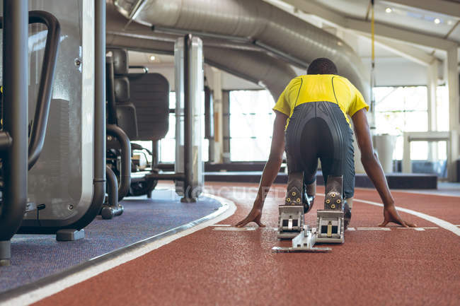 Visão traseira do atlético masculino afro-americano com deficiência no início do bloco na pista de corrida no centro de fitness — Fotografia de Stock