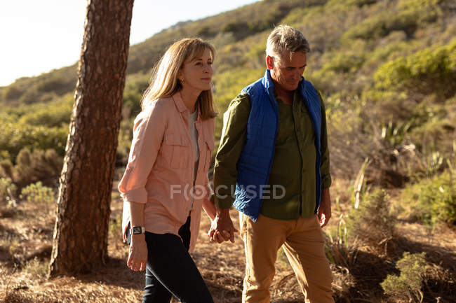 Vista lateral de perto de um homem e uma mulher caucasianos maduros de mãos dadas e andando durante uma caminhada — Fotografia de Stock