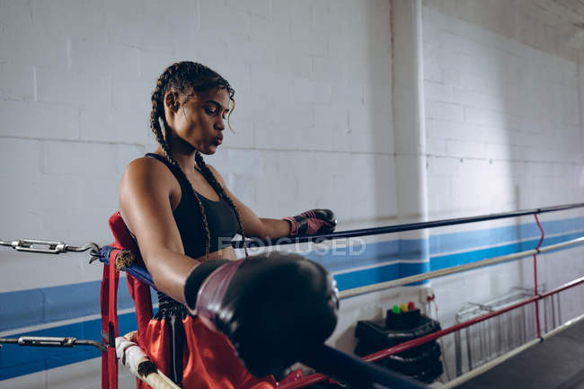 Side view of female boxer resting in the corner of the boxing ring at boxing club. Strong female fighter in boxing gym training hard. — Stock Photo