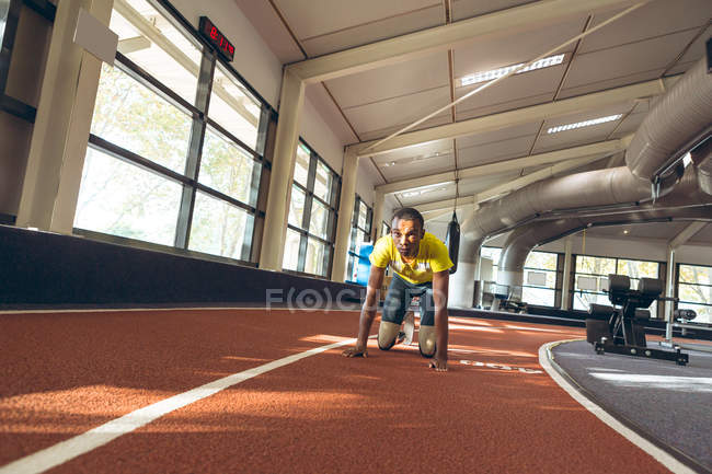 Vista frontal de un hombre afroamericano discapacitado relajándose en una pista de atletismo en el gimnasio - foto de stock