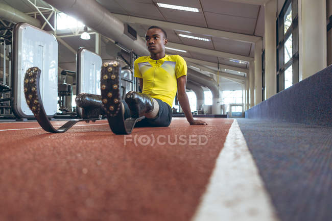 Vista frontale di un atletico afroamericano disabile che si rilassa su una pista da corsa nel centro fitness — Foto stock