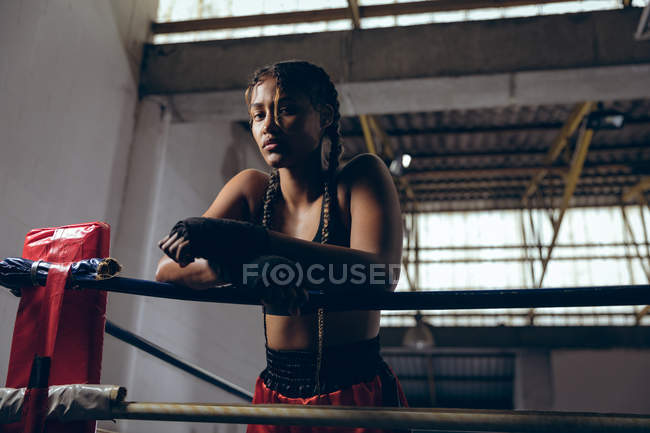 Tiefansicht einer Boxerin, die sich an Seile lehnt und im Boxring in die Kamera blickt. Starke Kämpferin im harten Boxtraining. — Stockfoto
