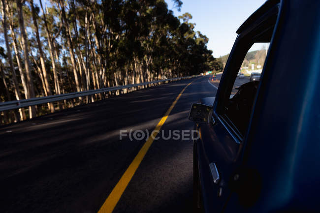 Rear view close up of the side of a pick-up truck in shadow, driving on a tree-lined highway — Stock Photo