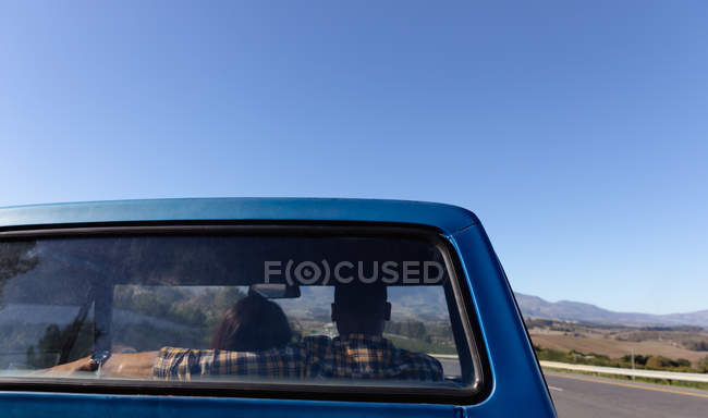 Rear view of a couple driving in a pick-up truck on a highway during a road trip, seen through the truck rear window — Stock Photo