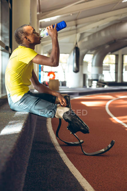 Вид сбоку на инвалида афроамериканского мужчины спортивной питьевой воды на ипподроме в фитнес-центре — стоковое фото