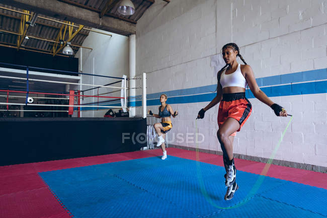 Front view of female boxers exercising with skipping rope in boxing club. Strong female fighter in boxing gym training hard. — Stock Photo