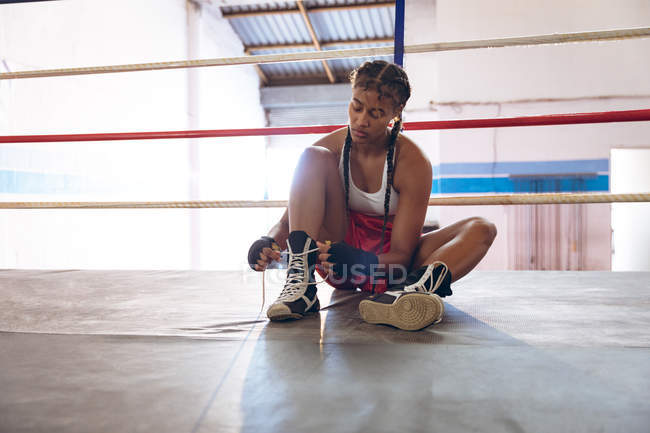 Front view of female boxer tying shoelaces in boxing ring at fitness center. Strong female fighter in boxing gym training hard. — Stock Photo