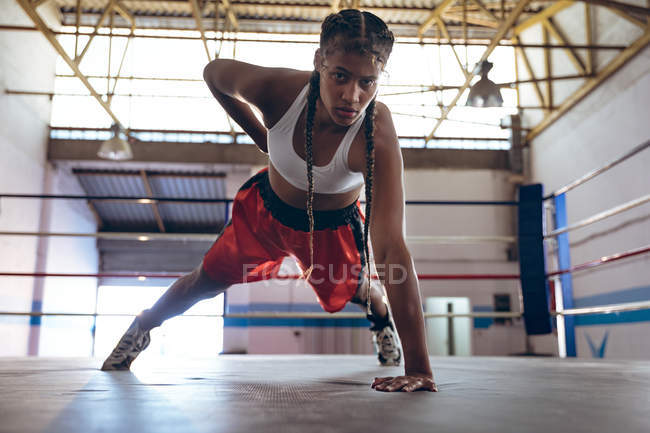 Boxer féminin regardant la caméra tout en exerçant dans le ring de boxe au centre de remise en forme. Forte combattante dans la boxe gymnase entraînement dur . — Photo de stock