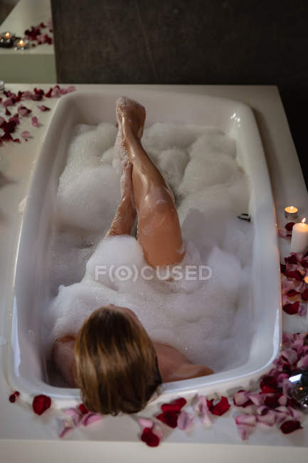 Elevated view of a young woman lying in a foam bath with lit candles and rose petals around it. — Stock Photo