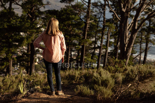 Rear view of a mature Caucasian woman stopping to enjoy the scenery in a forest, looking towards the sea during a hike — Stock Photo