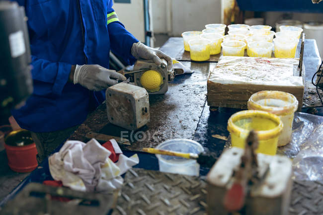 Vista lateral sección media de un hombre abriendo un molde para producir el núcleo de una bola en un taller en una fábrica de bolas de cricket . - foto de stock