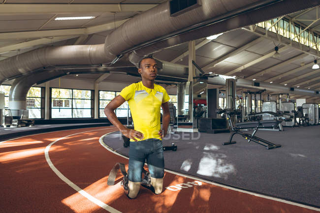 Vista frontale di un maschio afroamericano disabile inginocchiato con le mani sul fianco nel centro fitness — Foto stock