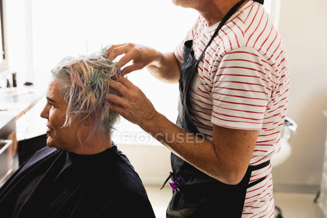 Side view close up of a middle aged Caucasian male hairdresser and a young Caucasian woman having her hair colored in a hair salon — Stock Photo