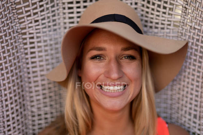 Retrato de una joven mujer caucásica feliz relajándose de vacaciones, usando un sombrero y sonriendo a la cámara - foto de stock