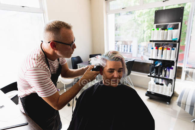 Передня картина середнього віку Кавказький самець перукаря і молода кавказька жінка, які стригли волосся в салоні для волосся. — стокове фото