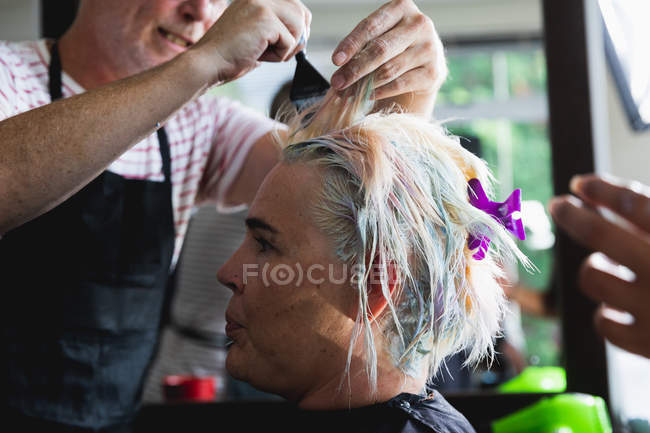 Nahaufnahme eines kaukasischen Friseurs mittleren Alters und einer jungen kaukasischen Frau mit gefärbten Haaren in einem Friseursalon — Stockfoto