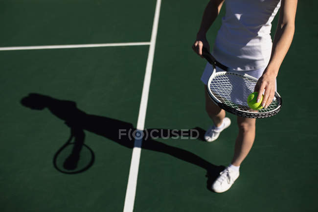 Вид спереду на жінку, яка грає в теніс в сонячний день, тримає ракетку і м'яч — стокове фото