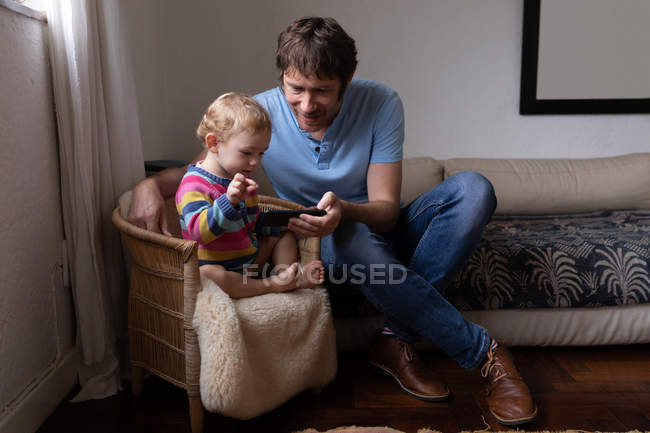 Вид спереди на молодого кавказского отца и его ребенка с помощью смартфона — стоковое фото