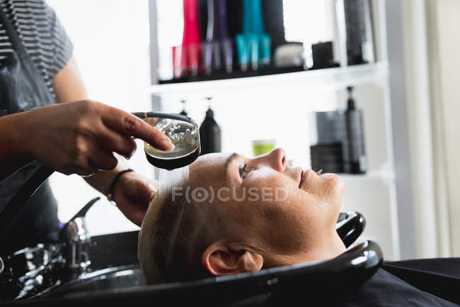 Вид сбоку на парикмахера и молодую кавказскую женщину с мытыми волосами в парикмахерской — стоковое фото