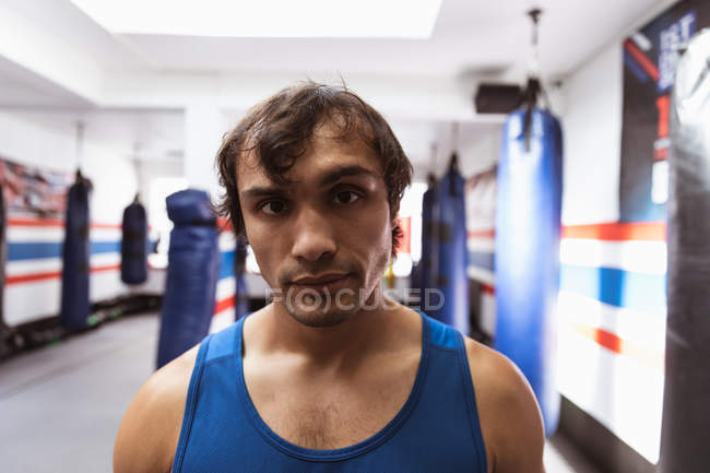 Retrato de cerca de un joven boxeador masculino de raza mixta en un gimnasio de boxeo mirando a la cámara - foto de stock