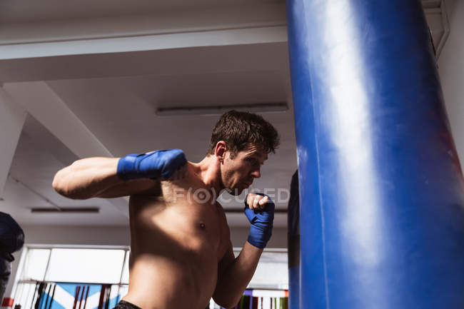 Vista lateral de perto de um jovem boxeador masculino caucasiano em um ginásio de boxe perfurando um saco de pancada — Fotografia de Stock