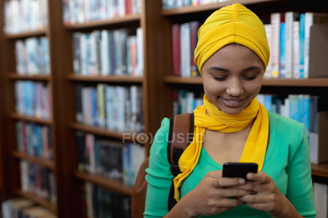 Вид спереди на молодую азиатскую студентку в хиджабе с помощью смартфона в библиотеке — стоковое фото
