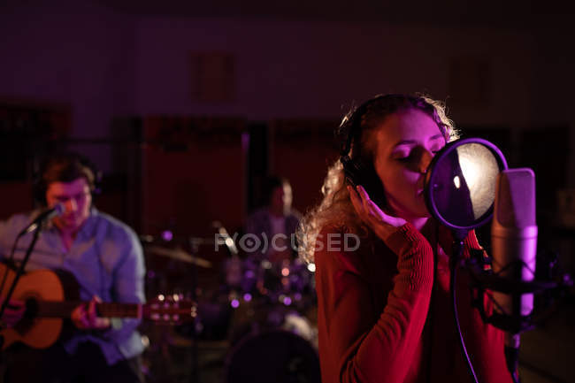 Front view of a young Caucasian female singer and a young Caucasian male singer guitarist performing during a session at a recording studio, with a drummer behind a drum kit in the background — Stock Photo