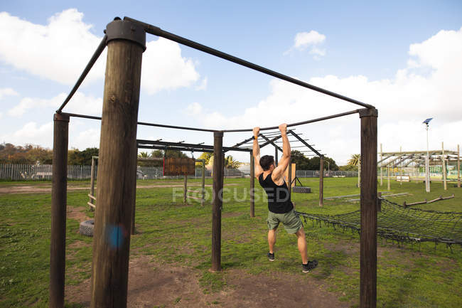 Visão traseira de um jovem caucasiano balançando em uma armação em um ginásio ao ar livre durante uma sessão de treinamento de bootcamp — Fotografia de Stock
