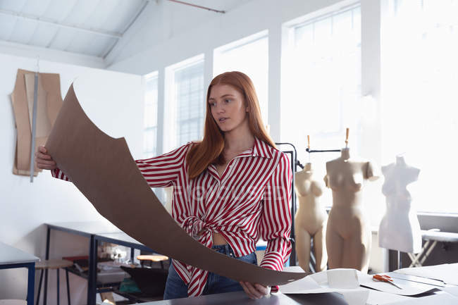 Vista frontale di una giovane studentessa di moda caucasica che tiene un modello mentre lavora su un design in uno studio al college di moda — Foto stock