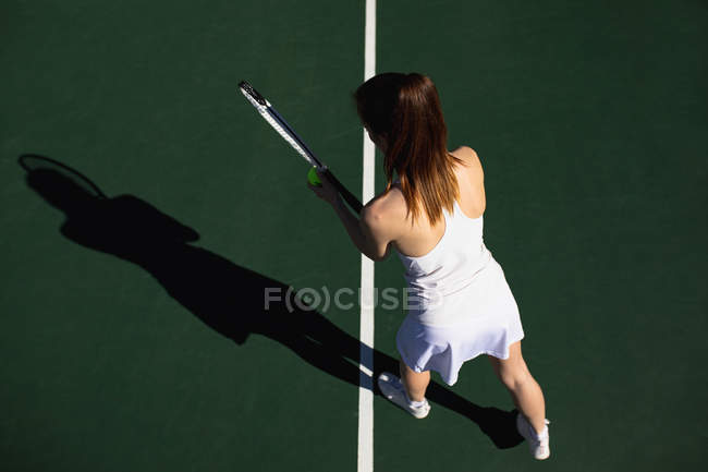 Vista trasera de una joven mujer caucásica jugando tenis en un día soleado, sirviendo - foto de stock