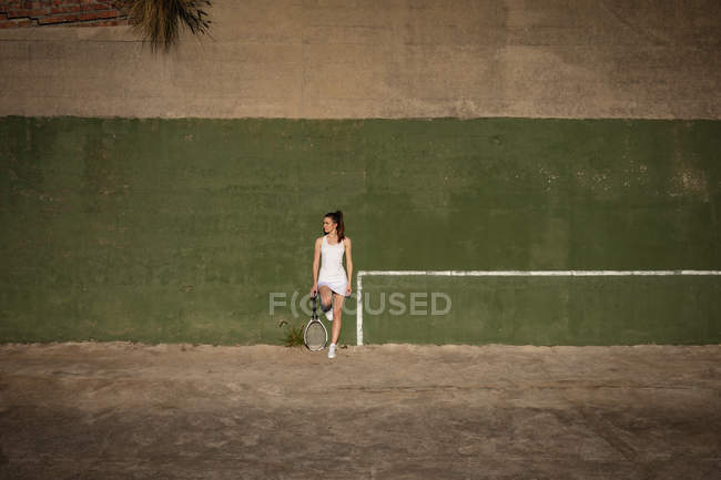 Вид спереди молодой кавказки, стоящей на теннисном корте со стеной за спиной — стоковое фото